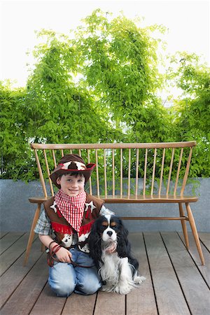 Boy (7-9) wearing cowboy costume, kneeling with dog on decking Stock Photo - Premium Royalty-Free, Code: 693-03309170