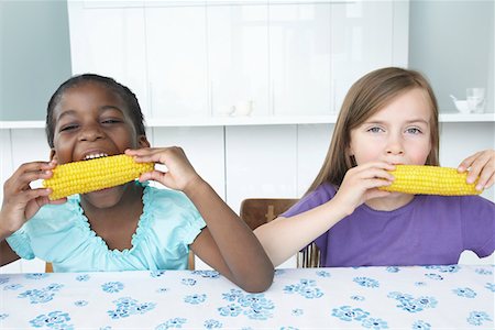 Two girls (5-6) sitting at table, eating corn cobbs Stock Photo - Premium Royalty-Free, Code: 693-03309187