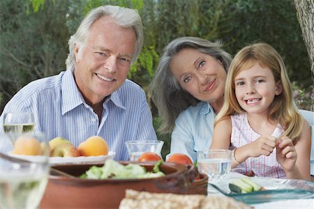 Grandparents with granddaughter (5-6) sitting at garden table, portrait Stock Photo - Premium Royalty-Free, Code: 693-03309278