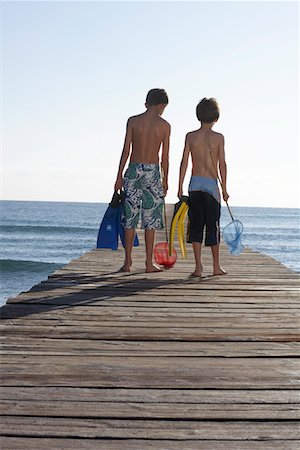 simsearch:693-03309303,k - Two boys (6-11) walking on jetty carrying fishing nets and swim fins, back view Stock Photo - Premium Royalty-Free, Code: 693-03309304