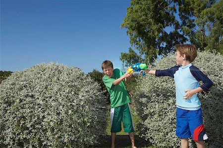 Two boys (6-11) playing with water pistols among bushes, laughing Stock Photo - Premium Royalty-Free, Code: 693-03309346