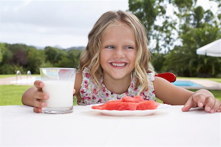 Portrait of girl (5-6) sitting at table with watermelon and glass of milk, laughing Stock Photo - Premium Royalty-Free, Code: 693-03309400