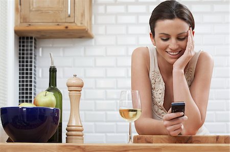 photo of apples in a white bowl - Young woman text messaging, leaning on kitchen counter Stock Photo - Premium Royalty-Free, Code: 693-03309681