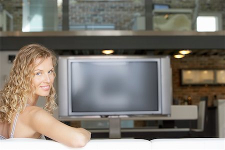 Woman sitting in modern living room, plasma television in background, portrait Stock Photo - Premium Royalty-Free, Code: 693-03300388