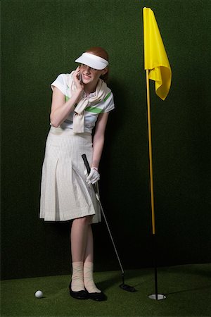 Woman in visor holding golf club by flag in hole Stock Photo - Premium Royalty-Free, Code: 693-03300679