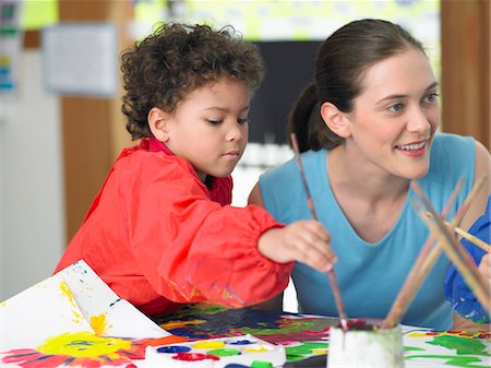 Art teacher squatting next to boy painting in art class Stock Photo - Premium Royalty-Free, Code: 693-03300723