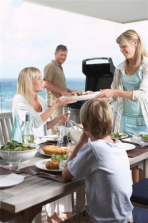 Family sitting around table outside eating Barbecue, father standing at grill grilling Stock Photo - Premium Royalty-Free, Code: 693-03300866