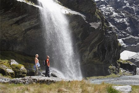 Hikers standing under waterfall at river Fotografie stock - Premium Royalty-Free, Codice: 693-03300998