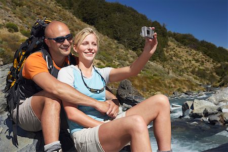 Man hugging woman as she takes their picture by a river in a forest Fotografie stock - Premium Royalty-Free, Codice: 693-03301012