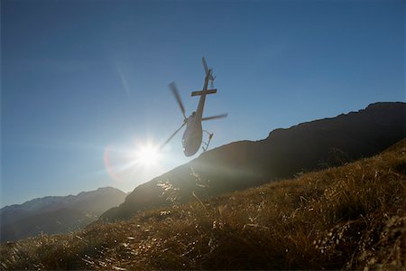 Helicopter flying over hills in front of the sun Stock Photo - Premium Royalty-Free, Code: 693-03301032