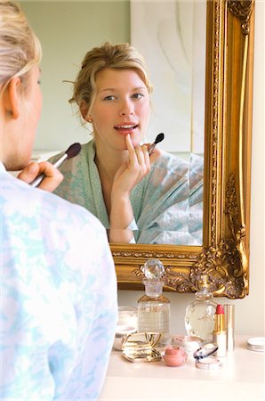 Woman in bathrobe sitting, Applying Make-up, looking in mirror Stock Photo - Premium Royalty-Free, Code: 693-03301286