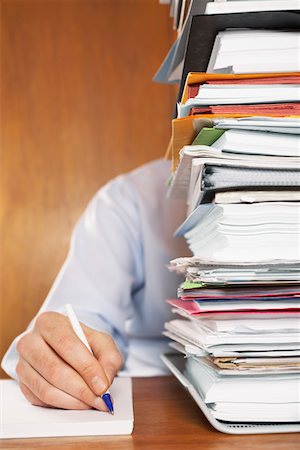 Man writing, close-up of arm and hand, sitting behind stack of paperwork at desk Stock Photo - Premium Royalty-Free, Code: 693-03301337