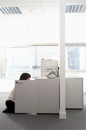 Female office worker kneeling in front of open cabinet in office, side view Stock Photo - Premium Royalty-Free, Code: 693-03301586