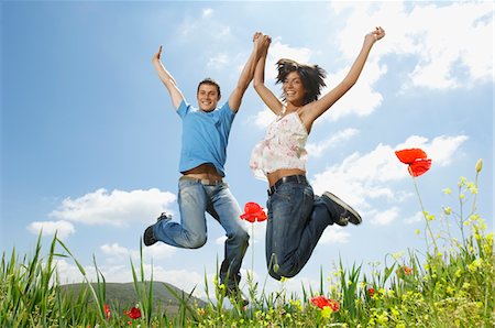 Young couple jumping for joy in mountain meadow, portrait, low angle view Stock Photo - Premium Royalty-Free, Code: 693-03301606