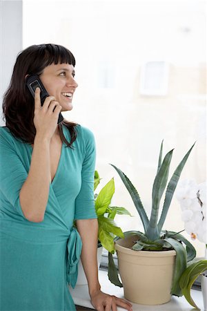 simsearch:693-03314647,k - Femme d'affaires souriant à l'aide du téléphone cellulaire de la plante et la fenêtre Photographie de stock - Premium Libres de Droits, Code: 693-03301756