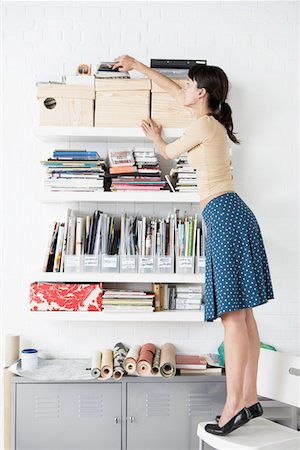 Businesswoman reaching for Shelf in home office Stock Photo - Premium Royalty-Free, Code: 693-03301761