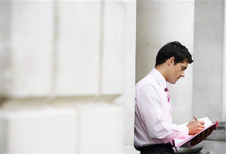 Businessman sitting against pillar outside building writing in notebook Stock Photo - Premium Royalty-Free, Code: 693-03301901