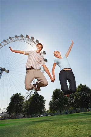 Young couple in park jumping in air in front of London Eye, portrait, low angle view Stock Photo - Premium Royalty-Free, Code: 693-03302153