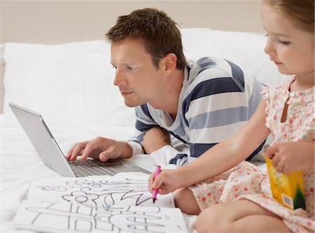 Father and daughter drawing and using laptop on bed Stock Photo - Premium Royalty-Free, Code: 693-03302332