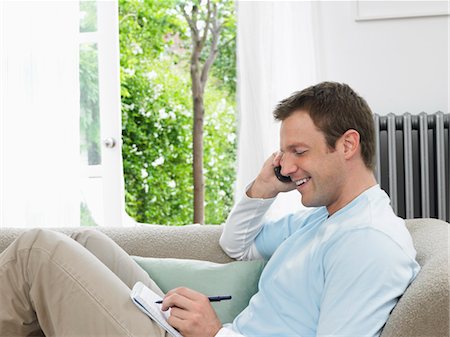 Man Using Cell Phone and Taking Notes Stock Photo - Premium Royalty-Free, Code: 693-03302345