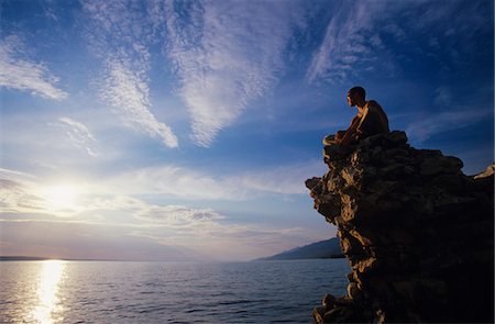 Man sitting on rock overlooking ocean Stock Photo - Premium Royalty-Free, Code: 693-03302476
