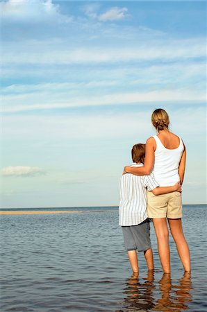 sad pic boy in water - Mother and Son standing in water by shore of Beach looking at view, back view Foto de stock - Sin royalties Premium, Código: 693-03303117