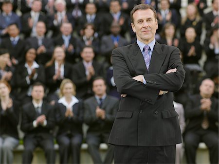 Business man standing in front of business people sitting on tribune, portrait Stock Photo - Premium Royalty-Free, Code: 693-03303484