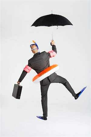 Middle-aged businessman in flippers, inflatable rubber ring, snorkel and goggles waddling, carrying briefcase and umbrella, back view Foto de stock - Sin royalties Premium, Código: 693-03303656