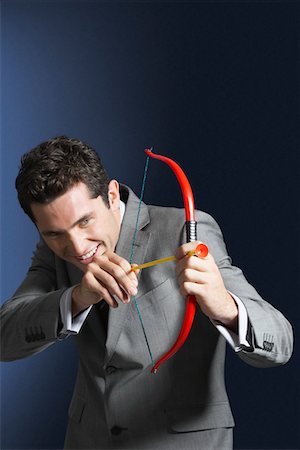 Man aiming toy bow and arrow against dark background Stock Photo - Premium Royalty-Free, Code: 693-03303793