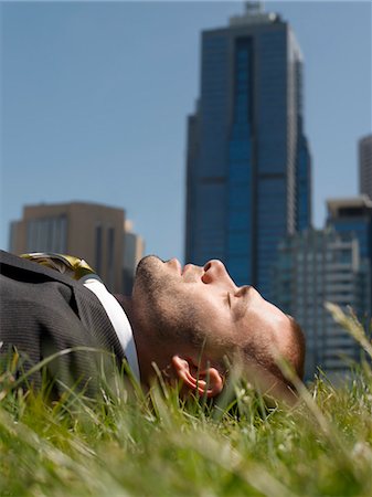 Business man lying on grass, office buildings in background Stock Photo - Premium Royalty-Free, Code: 693-03303817