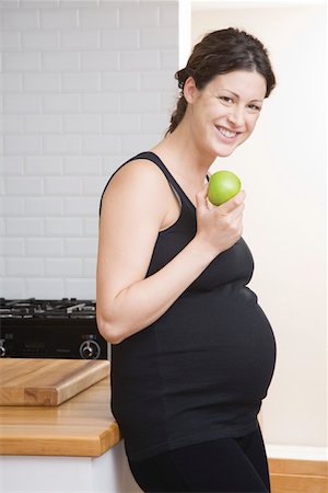 simsearch:693-03315753,k - Pregnant woman eating apple in kitchen, portrait Stock Photo - Premium Royalty-Free, Code: 693-03314550