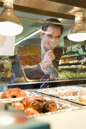 Mature man grins through glass of meat counter in supermarket Stock Photo - Premium Royalty-Free, Code: 693-03315622