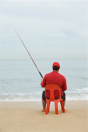 Man in red tshirt fishing from red plastic chair, Cape Town, South Africa Stock Photo - Premium Royalty-Free, Code: 693-03317536