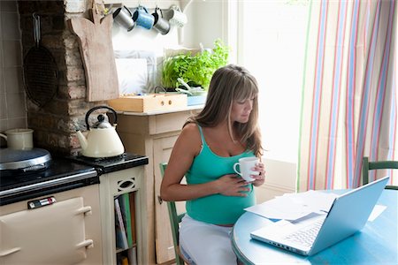 Femme enceinte, assis à la table de cuisine avec ordinateur portable Photographie de stock - Premium Libres de Droits, Code: 693-03317746