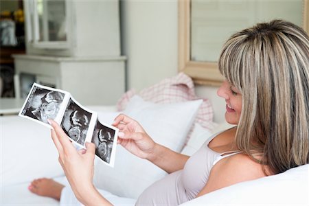 pregnant, ultrasound - Pregnant woman sitting on sofa with baby scan Foto de stock - Sin royalties Premium, Código: 693-03317756