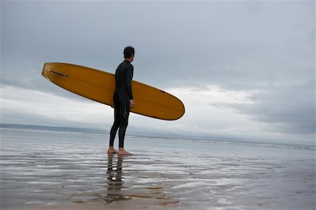 Surfer carrying surfboard on beach, side view, low angle view Stock Photo - Premium Royalty-Free, Code: 693-03310130