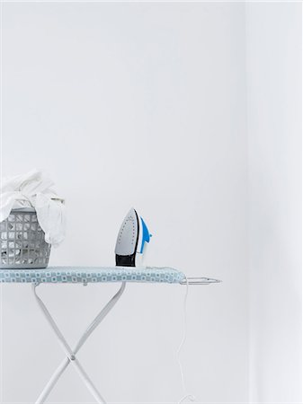 ferro de passar roupas - Iron and laundry basket on ironing board against white wall Foto de stock - Royalty Free Premium, Número: 693-03310988
