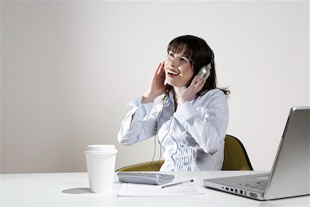 Smiling woman with earphones sitting at desk Stock Photo - Premium Royalty-Free, Code: 693-03311039