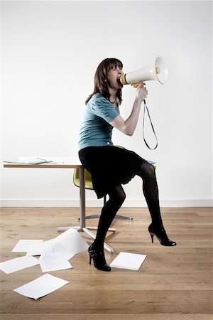 Woman sitting on desk, shouting through megaphone Stock Photo - Premium Royalty-Free, Code: 693-03311044