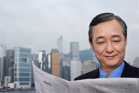 Middle-aged business man reading newspaper, office buildings in background Stock Photo - Premium Royalty-Free, Code: 693-03311567