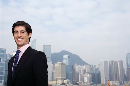 Portrait of young business man smiling, office buildings in background Stock Photo - Premium Royalty-Free, Code: 693-03311571