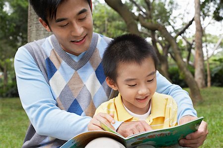 Father and son (7-9) reading book in park Stock Photo - Premium Royalty-Free, Code: 693-03311643