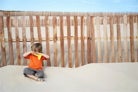sitting sad boy - Boy (3-4) covering eyes, sitting against wooden fence on sand dune Stock Photo - Premium Royalty-Free, Code: 693-03311843