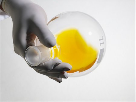 Person wearing rubber gloves mixing yellow liquid in lab flask, close up, studio shot Foto de stock - Sin royalties Premium, Código: 693-03311878