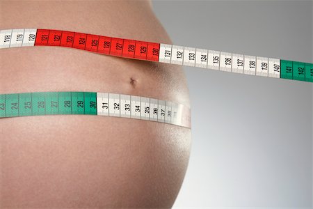 Pregnant woman with tape measure around abdomen, mid section, close up, studio shot Stock Photo - Premium Royalty-Free, Code: 693-03312017