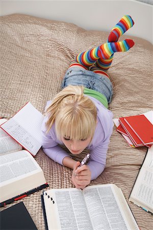 Teenage girl (16-17) doing homework lying on bed Stock Photo - Premium Royalty-Free, Code: 693-03312495
