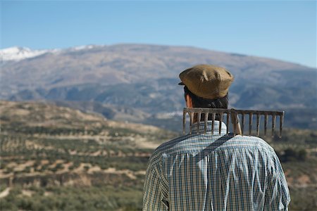 Farmer with rake on shoulder looking at orchard, back view Stock Photo - Premium Royalty-Free, Code: 693-03312659