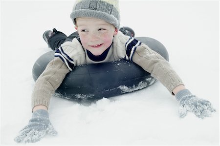 Boy in winter clothing sledging on an inner tyre Stock Photo - Premium Royalty-Free, Code: 693-03440906