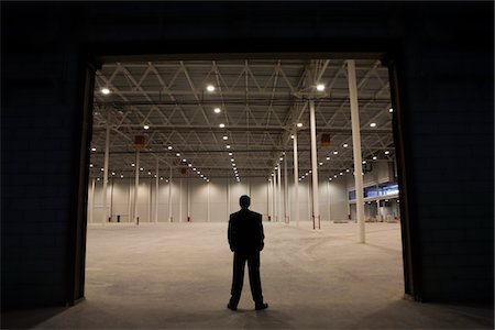suit man standing backside - Man stands with hands in pockets at warehouse entrance Foto de stock - Sin royalties Premium, Código: 693-03474174