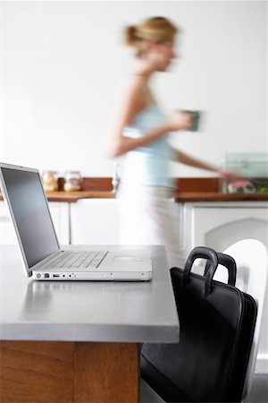 Woman in kitchen walking by laptop, focus on laptop Stock Photo - Premium Royalty-Free, Code: 693-03557245